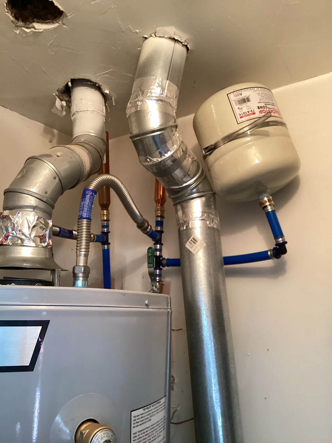 Water heater supply connections, expansion tank, and vent piping above a storage tank